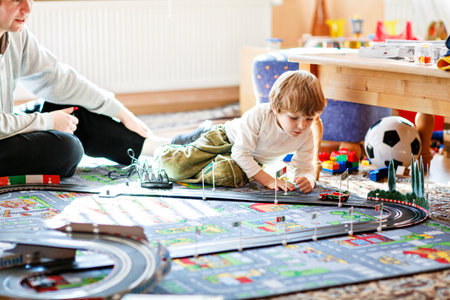 Father and son playing with racing cars on racetrack, indoors, with cars. Happy little preschool boy and young man having fun with indoor race gameの写真素材