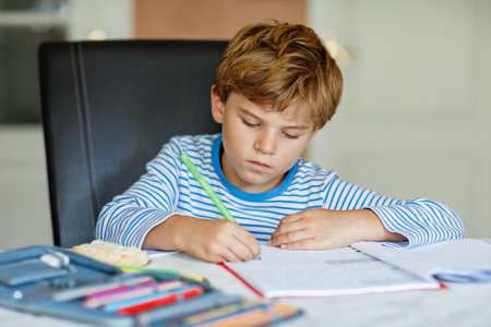 Portrait of cute healthy happy school kid boy at home making homework. Little child writing with colorful pencils, indoors. Elementary school and education. Kid learning writing letters and numbersの写真素材