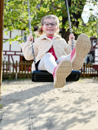 Adorable little girl having fun on a swing. Happy child on playground on sunny dayの写真素材