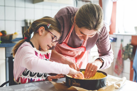 Little cute girl helps her mother bake a cake in the kitchen. Child and woman mixing ingredients...