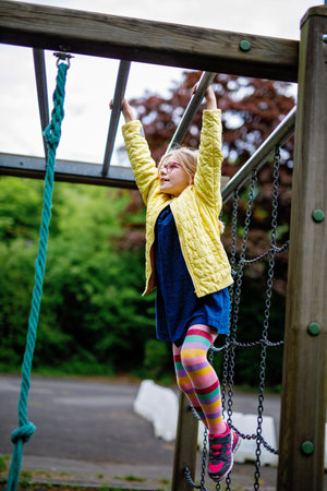Little girl doing gymnastics on a climbing frame, horizontal bar on school yard. Child enjoying...