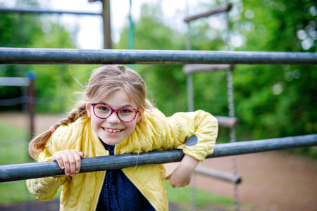Little girl doing gymnastics on a climbing frame, horizontal bar on school yard. Child enjoying school break.の写真素材