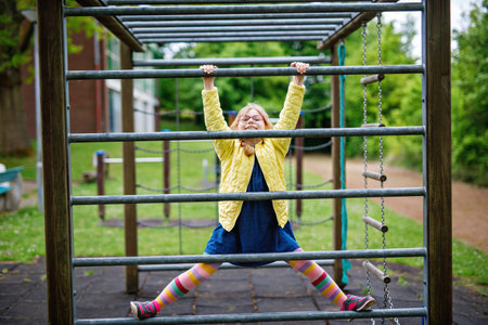 Little girl doing gymnastics on a climbing frame, horizontal bar on school yard. Child enjoying...