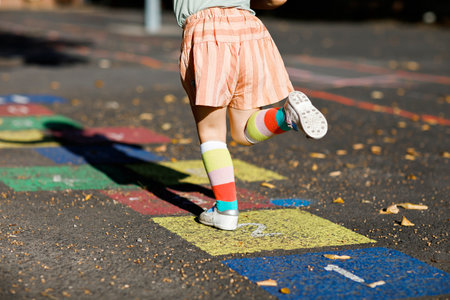 Closeup of leggs of little toddler girl playing hopscotch game drawn with colorful chalks on asphalt. Little active child jumping on playground outdoors on a sunny day. Summer activities for children.の写真素材