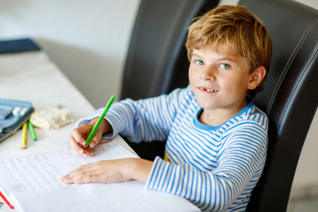 Portrait of cute healthy happy school kid boy at home making homework. Little child writing with colorful pencils, indoors. Elementary school and education. Kid learning writing letters and numbersの写真素材