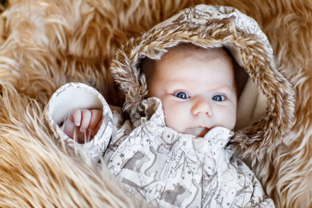 Portrait of newborn baby in warm winter clothes. Beautiful cute girl in warm overall, cap. Peaceful...