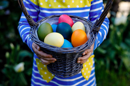 Close-up of of hands of toddler holding basket with colored eggs. Child having fun with traditional...