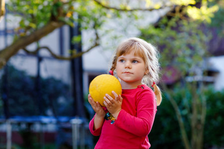 Little adorable toddler girl playing with ball outdoors. Happy smiling child catching and throwing, laughing and making sports. Active leisure with children and kids.の写真素材