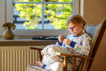 Little girl sewing a pillow for her stuffed animal. Happy Child sitting next to a window holding a needle and yarnの写真素材