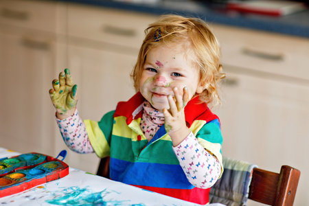 Cute adorable baby girl learning painting with water colors. Little toddler child drawing at home, using colorful brushes. Healthy happy daughter experimenting with colors, water at home or nursery.の写真素材