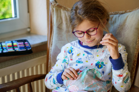 Little girl sewing a pillow for her stuffed animal. Happy Child sitting next to a window holding a needle and yarnの写真素材