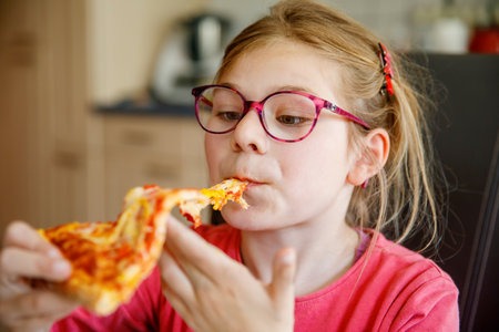 Little school Girl eating a piece of Pizza. Happy Child biting pizza with tomato and cheese.の写真素材