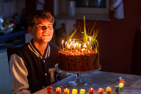 Adorable happy teenage kid boy celebrating his birthday. Teenager child blowing 14 candles on homemade baked cake, indoor. Birthday party for school children, family celebration, teenager birthdayの写真素材