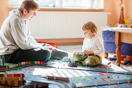 Father and son playing with racing cars on racetrack, indoors, with cars. Happy little preschool boy and young man having fun with indoor race gameの写真素材