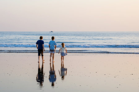 Three children, happy siblings on ocean beach at sunset. happy family, two school boys and one little preschool girl. Brothers and sister having funの写真素材