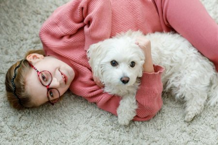 Little girl playing with her pet dog Maltese at home. Happy child and cute puppy. Love, friendship, family animal.の写真素材