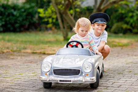 Two happy children playing with big old toy car in summer garden, outdoors. Kid boy driving car with little toddler girl inside. Laughing and smiling kids. Family, childhood, lifestyle conceptの写真素材