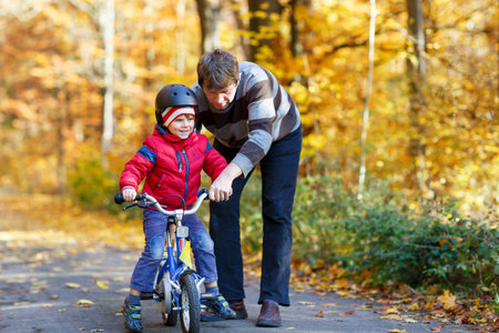 Little kid boy and his father in autumn park with a bicycle. Dad teaching his son bikingの写真素材
