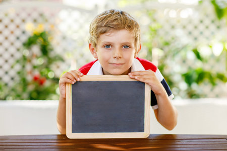 Happy little kid boy with chalk desk in hands. Healthy adorable child outdoors . Empty chalk desk with copy space for text.の写真素材
