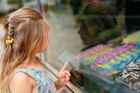 Happy preschool girl choosing and buying ice cream in outdoor stand cafe. Cute child looking at different sorts of icecream. Sweet summer dessert on family vacations. Summertime.の写真素材