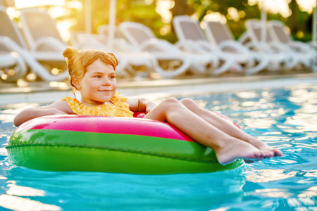 Happy little girl with inflatable toy ring float in swimming pool. Little preschool child learning to swim and dive in outdoor pool of hotel resort. Healthy sport activity and fun for children.の写真素材