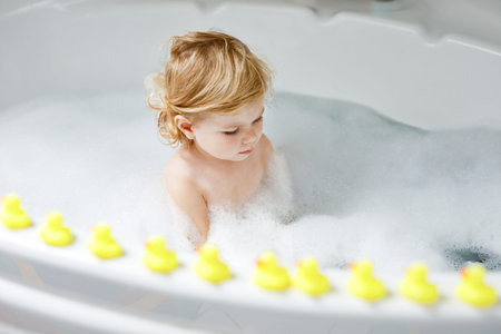 Adorable cute little toddler girl taking bath in bathtub. Happy healthy baby child playing with...