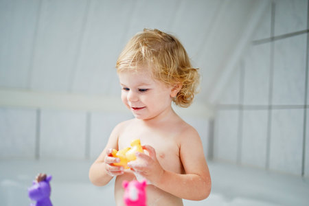 Adorable cute little toddler girl taking bath in bathtub. Happy healthy baby child playing with rubber gum toys and having fun. Washing, cleaning, hygiene for children.の写真素材