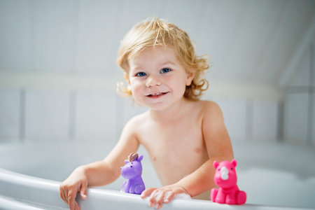 Adorable cute little toddler girl taking bath in bathtub. Happy healthy baby child playing with...