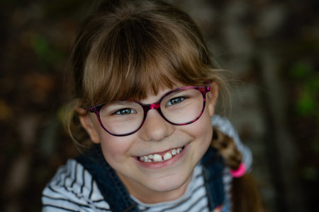 Portrait of cute, happy, smiling elementary school girl with eyeglasses and long blond hair. Real...