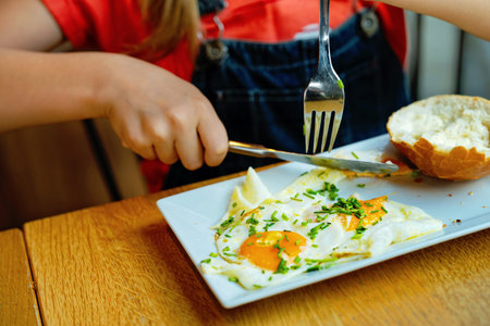 Adorable little elementary school girl with glasses having breakfast in a cozy cafe. Child eating...