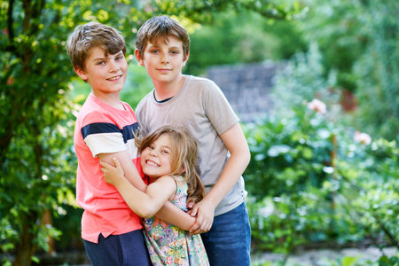 Portrait of three siblings children. Two kids brothers boys and little cute toddler sister girl having fun together in domestic garden. Happy healthy family playing, walking, active leisure on natureの写真素材