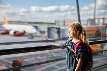 Little girl at the airport waiting for boarding at the big window. Cute kid stands at the window against the backdrop of airplanes. Looking forward to leaving for a family summer vacationの写真素材