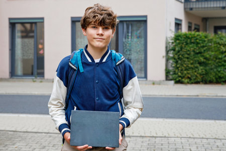 Teenage school boy with backpack holding sign chalk desk, empty, for copyspace for text standing outdoors. Student on first school day after summer vacation.の写真素材