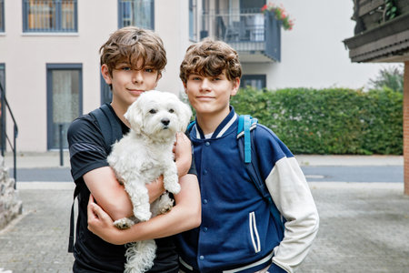 Two teenage kid boys with backpack or satchel. Schoolkids on the way to school. Healthy smiling children, brothers and best friends outdoors on the street leaving home. Back to school. Happy siblings.の写真素材