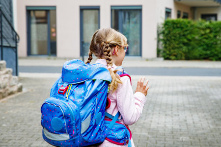 Happy little elementary school girl with eyeglasses and satchel backpack walking outdoors on the way to school. Smiling pupil child ready for back to school, education and childhood lifestyle concept.の写真素材