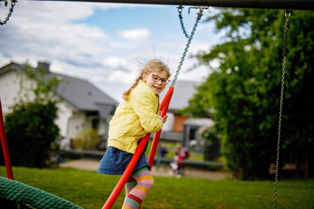 Little school girl swinging on big chain swing on school yard. Happy child enjoying school breakの写真素材
