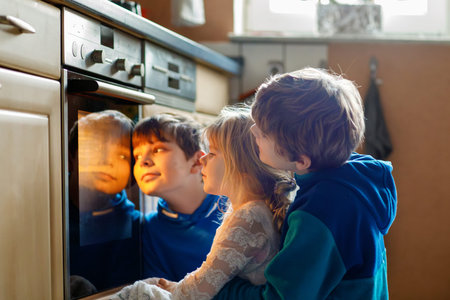 Little toddler girl and two kids boys baking pumpkin cake or cookies in kitchen. Three children,...