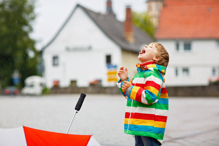 Little toddler boy playing on rainy day. Happy positive child having fun with catching rain drops. Kid with rain clothes. Children and family outdoor activity on bad weather day.の写真素材