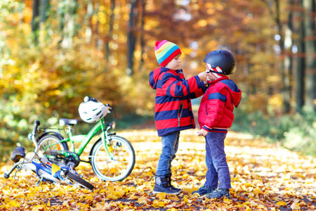 Two little kid boys with bicycles in autumn forest putting helmetsの写真素材