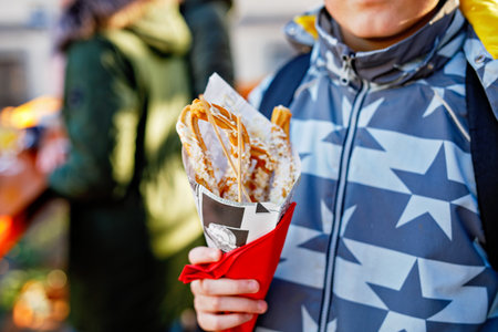 Happy teenager boy eating churros sweets covered with chocolate with decoration and lights on background. Happy child on Christmas market in Germany.の写真素材