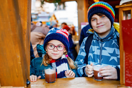 Little cute school girl and teenag boy drinking hot chocolate on German Christmas market. Happy children, siblings on traditional family market in Germany, Laughing kids in colorful winter clothesの写真素材
