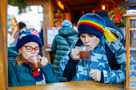 Little cute school girl and teenag boy drinking hot chocolate on German Christmas market. Happy children, siblings on traditional family market in Germany, Laughing kids in colorful winter clothesの写真素材