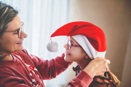 Family, celebration, holiday. Happy mother hugging her little girl child in santa hat. Cute happy school girl with eye glasses having fun.の写真素材