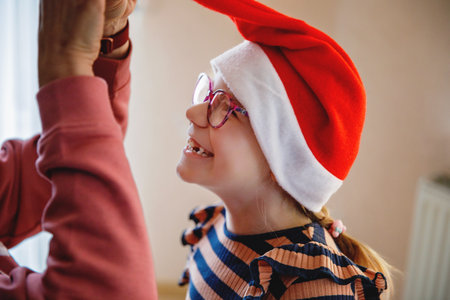 Family, celebration, holiday. Happy mother hugging her little girl child in santa hat. Cute happy school girl with eye glasses having fun.の写真素材
