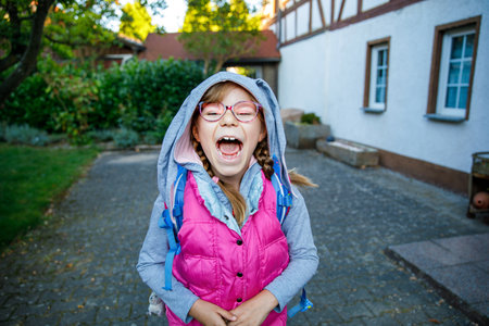 Happy little elementary school girl with eyeglasses and satchel backpack walking outdoors on the way to school. Smiling pupil child ready for back to school, education and childhood lifestyle concept.の写真素材