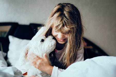 Adorable little girl sleeping and playing with cute Maltese dog in the bed. Happy child and beloved pet together indoors. Childhood, friendship, family and love for animals concept.の写真素材