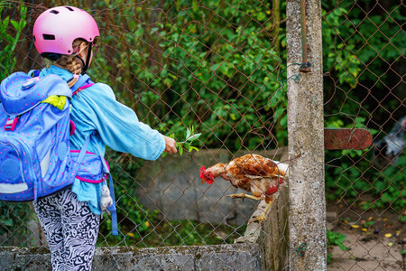 Happy elementary school girl riding a scooter to school wearing a helmet and backpack. Safe, active, real-life cute child commuting in the city.の写真素材
