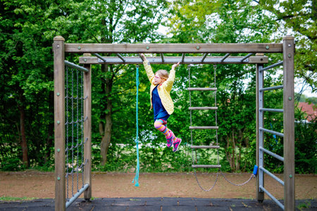 Little girl doing gymnastics on a climbing frame, horizontal bar on school yard. Child enjoying...
