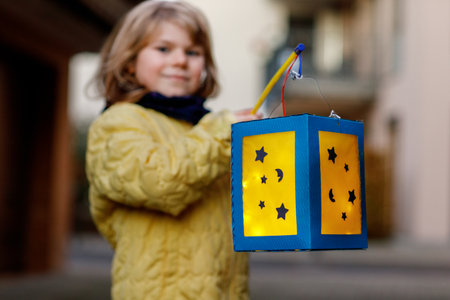 Little Preschool Kid Girl Holding Selfmade Traditional Lanterns with Candle for St. Martin Procession. Child Happy about Children and Family Parade in Kindergarten. German tradition St. Martin's paradeの写真素材