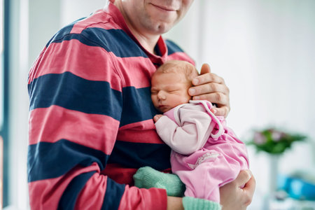 Happy father holding his newborn baby girl in arms. Cute little infant sleeping peacefully on dad...